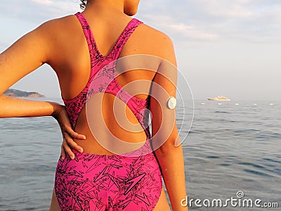 Girl with diabetes enters the sea. On the right arm is placed white sensor for continuous glucose monitoring in blood â€“ CGM Stock Photo