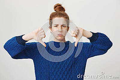 Girl disagree and shows her condemn. Studio shot of displeased frowning redhead european girl in bun and winter sweater Stock Photo