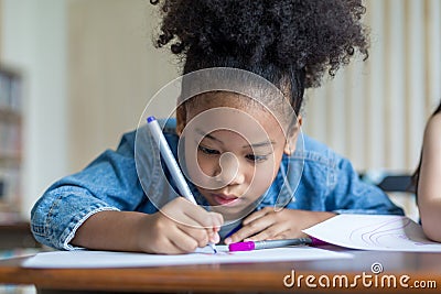 Girl is doing homework in the Classroom. Back to school! Cute industrious children are sitting at desks indoors. Kids are learning Stock Photo