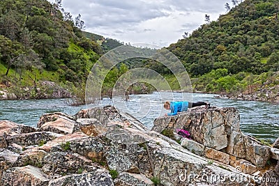 Girl Doing a Plank on Rocks Near Fast River Stock Photo