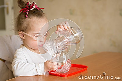 Girl with Down syndrome gently pours water from a jug into a jug Stock Photo