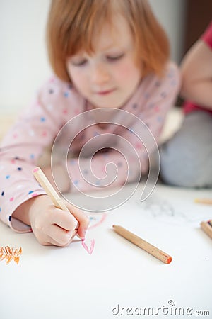 Girl draws with colored pencils lying on the floor Stock Photo