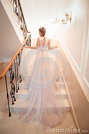 A girl in a dress climbs the stairs. Beautiful lady in a luxurious ball gown climbing the stairs. Baluster railing on both sides. Stock Photo