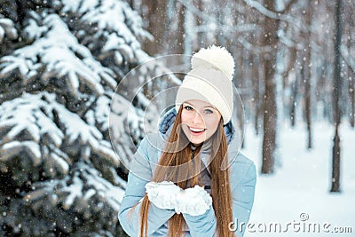 A girl dressed in warm winter clothes and a hat posing in a winter forest. Model with a beautiful smile near the Christmas tree. Stock Photo