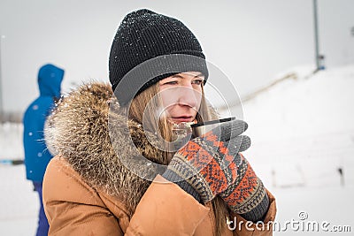 Girl drinking hot tea in the winter forest portrait. A young in warm clothes holding cup with drink on the background of the Stock Photo