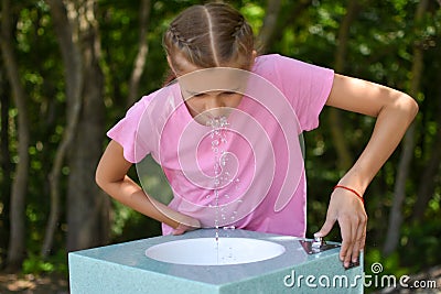 Girl drinks clean water in a fountain, quench her thirst in the heat. Stock Photo