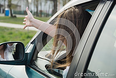 A girl drives a car and swears, shows her hand through the window to another driver or pedestrian. Woman driving Stock Photo