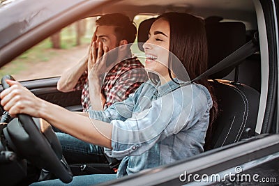 Girl is driving car and laughing. Guy is sitting besides her. He is terrified because of his girlfriend`s driving. Young Stock Photo