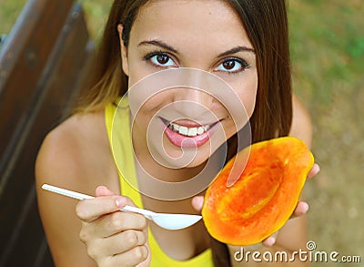 Girl eating healthy papaya in the park looking at camera. Woman eating tropical fresh fruit outdoor. Stock Photo