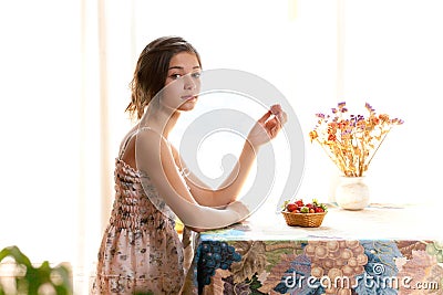 Girl eating strawberries sitting at table indoor Stock Photo