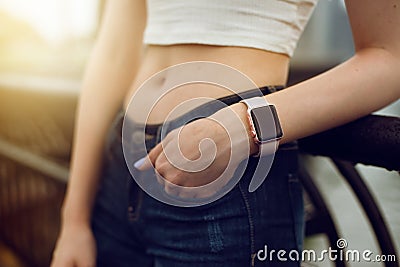 Girl with electronic watch holding hand at jeans pocket in city at sunset time. Stock Photo