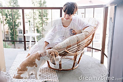 Girl with elegant white manicure stroking beagle dog while enjoying coffee in morning. Gorgeous young lady in summer Stock Photo