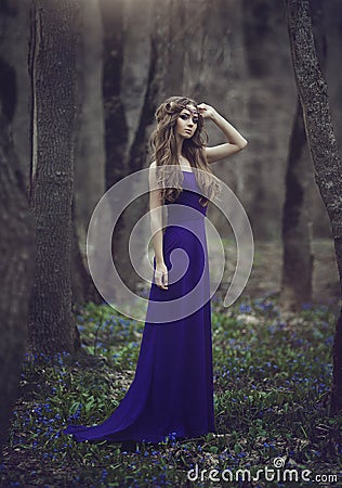 Girl elf with long hair and blue eyes in tiara and a long blue dress with a train walking through the spring blossoming Stock Photo