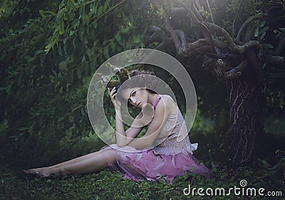 Girl enchanted Princess with horns sitting under a tree. Girl Mystical creature fawn in shabby clothes in a fairy forest Stock Photo