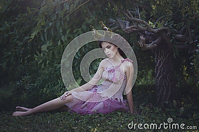 Girl enchanted Princess with horns sitting under a tree. Girl Mystical creature fawn in shabby clothes in a fairy forest Stock Photo