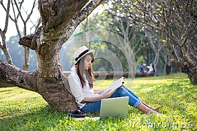 Girl enjoy reading a book under the tree, laying on grass of park Stock Photo
