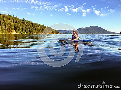 A girl enjoying kayaking on the beautiful and calm ocean waters of Howe Sound, off of Gambier Island, British Columbia, Canada. Stock Photo