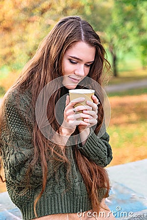 Girl enjoys smell of coffee sitting in autumn park Stock Photo