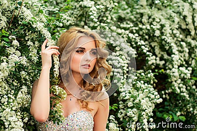 Girl in evening cocktail dress on a spring in the middle among flowering bushes and trees beautiful smiling Stock Photo