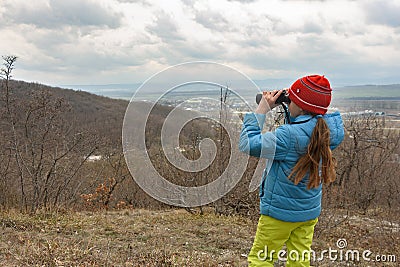 A girl examines a mountain landscape through binoculars, view from the back Stock Photo