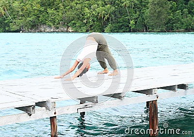 Girl exercising yoga pose downward-facing dog on jetty by sea Stock Photo