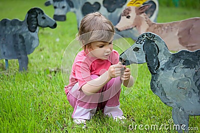 The girl feeds wooden sheep Stock Photo