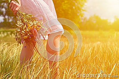 Girl in a field with a bunch of wild flowers in their hands. The concept of purity and unity with nature, sunlight Stock Photo