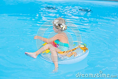 Girl with flowers frangipani on her head in her hair floating on the circle in the pool on a sunny day Stock Photo