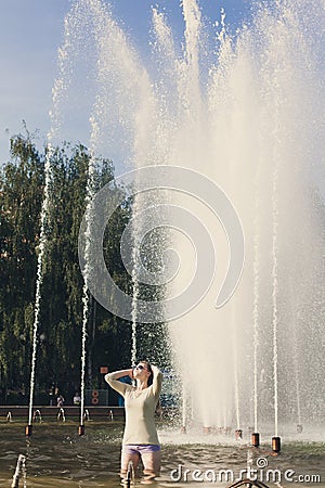 Girl with flowing hair in short shorts and sunglasses is standing in the fountain Stock Photo