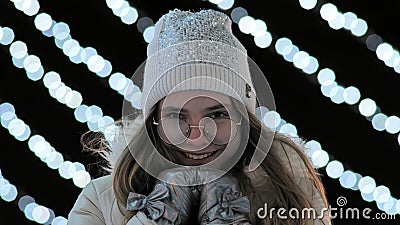 The girl freezes in the evening in the city in winter against the background of gerlands. Stock Photo