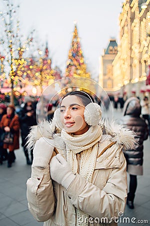 Girl in fur hood headphones in Christmas market decorated with holiday lights in the evening. Christmas tree lights on background Stock Photo