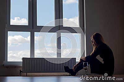A girl with a glass of wine sits on the floor at a large stained glass window Stock Photo