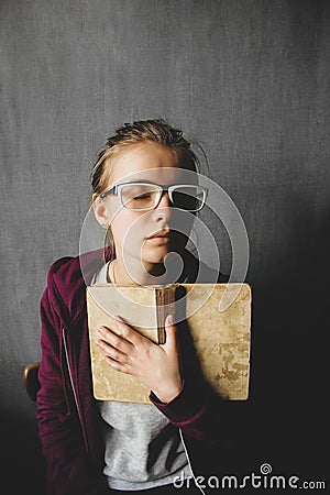Girl in glasses with a book on a gray background. The girl is holding an old book Stock Photo