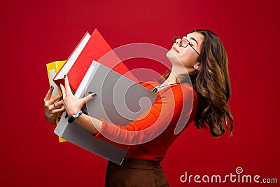 The girl in glasses carries folders, with a fright on her face on a red background. Mood stress, panic, accounting reporting, tax Stock Photo