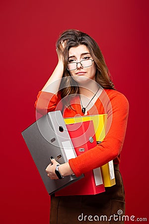 The girl in glasses carries folders, with a panic on her face on a red background. Mood stress, accounting reporting, tax audit, Stock Photo