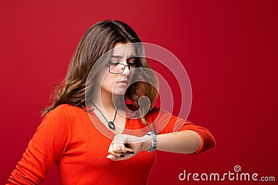 The girl in glasses looks at the watch. Hurry up. Appreciate your time. Do not be late. Isolated on red background Stock Photo