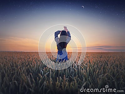 Girl in the golden wheat field at sunset. Beautiful twilight scenery under the summer starry sky with crescent moon. Magical Stock Photo