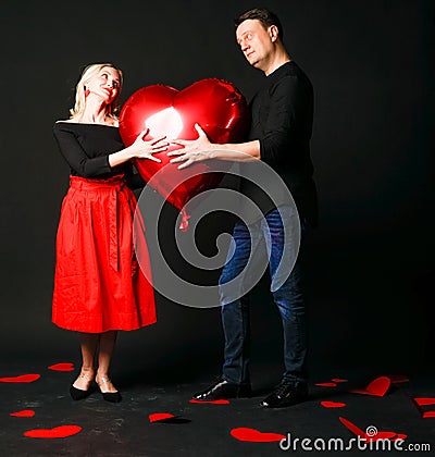 A girl and a guy hold a heart balloon inflatable valentine, happiness flirt, on the floor hearts are a beautiful layout Stock Photo