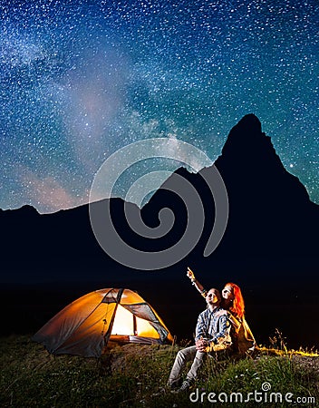 Girl and guy looking at the shines starry sky at night. Couple sitting near camping Stock Photo