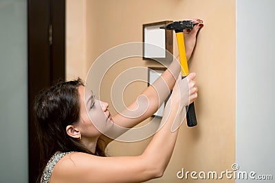 Girl hammer a nail into the wall to hang a photo frame Stock Photo