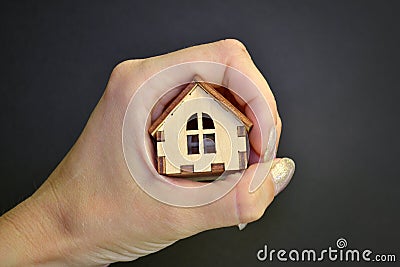 Girl hand holding in fist wooden miniature toy house on a light with black background, with a copyspace Stock Photo