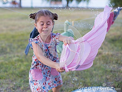 Horizontal photo of a six year old girl who hangs laundry in the yard in summer Stock Photo