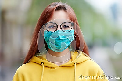 A girl with happy eyes, glasses in a reusable blue medical mask stands straight and looks straight Stock Photo