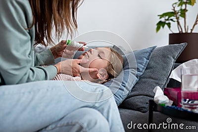 Girl has a runny nose and her mother sprays medicine into her nose Stock Photo