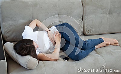The girl has a stomachache. A woman lies on the couch, is sick, she has a stomach ache. Abdominal pain Stock Photo