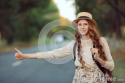 Girl with hat and backpack hitchhiking on the road Stock Photo