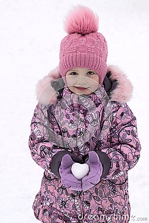 Girl in hat, coat and mittens holding a snowball in the shape of a heart. Stock Photo