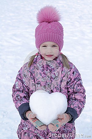 Girl in hat, coat and mittens holding a snowball in the shape of a heart. Stock Photo