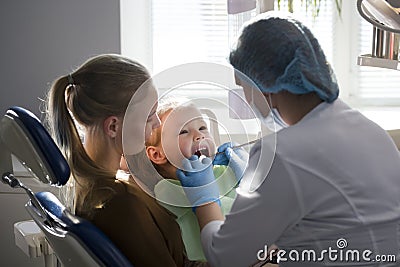 Girl, her mom and the dentist in the dental office, the stomatologist examining the girl using special instruments Stock Photo