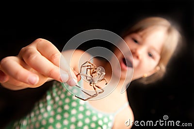 Girl holding brown spider by one leg and looking Stock Photo